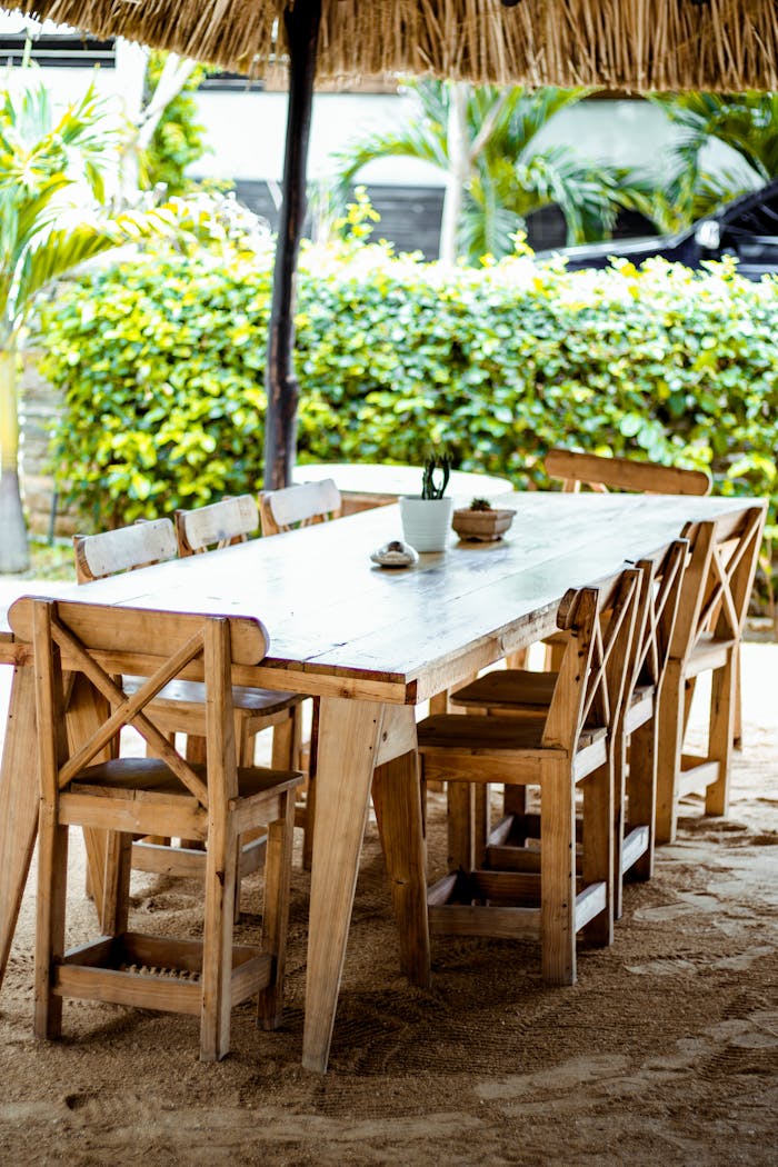 Wooden table and chairs under a thatched roof in a lush outdoor setting.