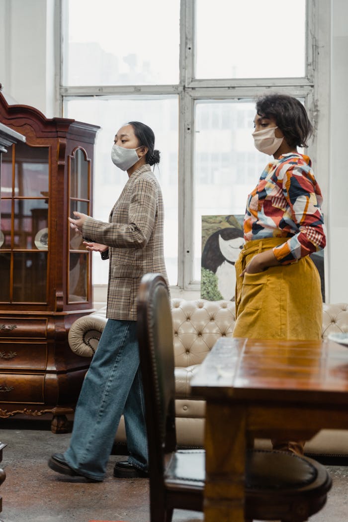 Two women wearing masks shop for antiques in a stylish store setting.